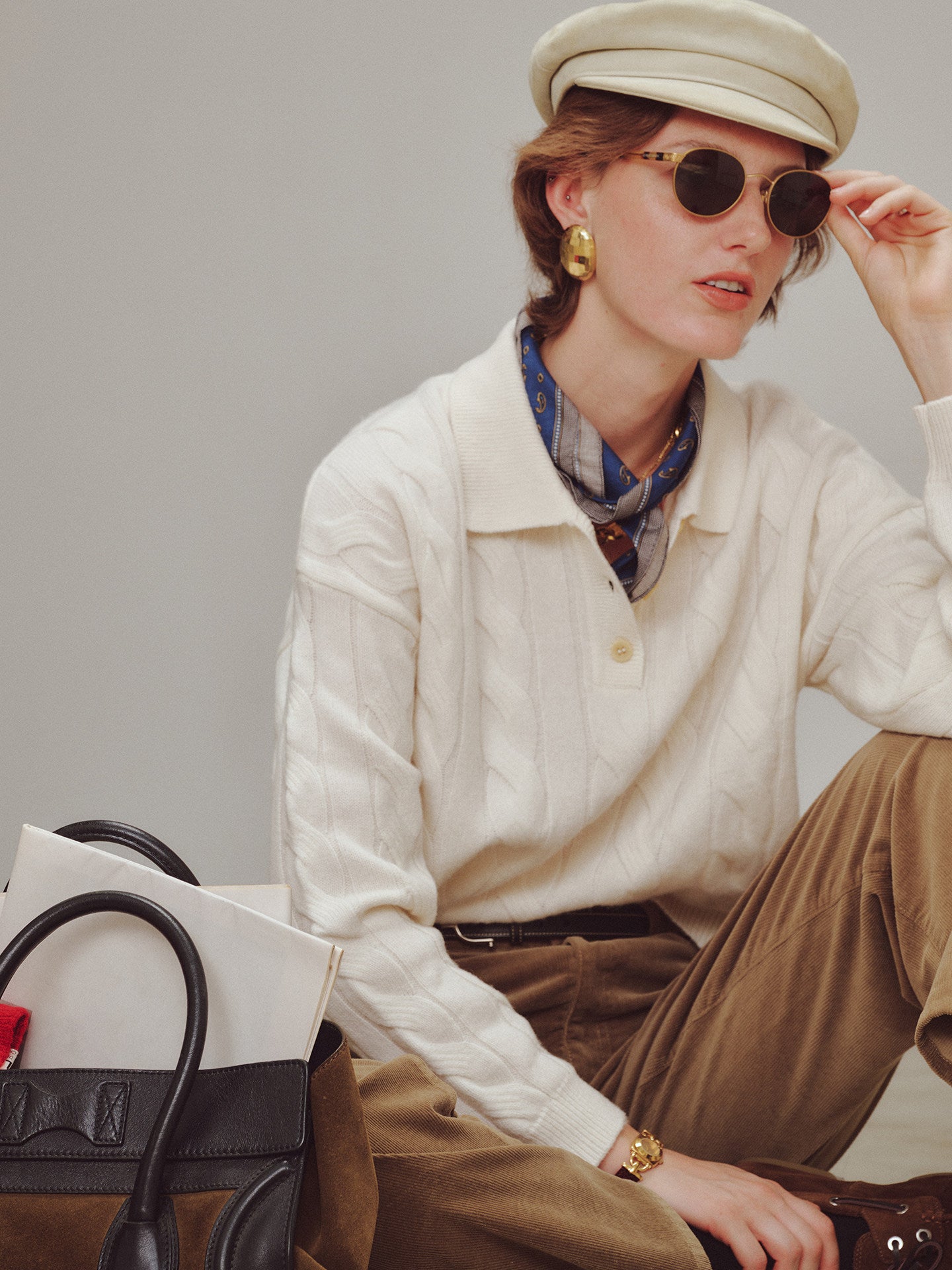 Person wearing a cream sweater, beige cap, and sunglasses with a gray background
