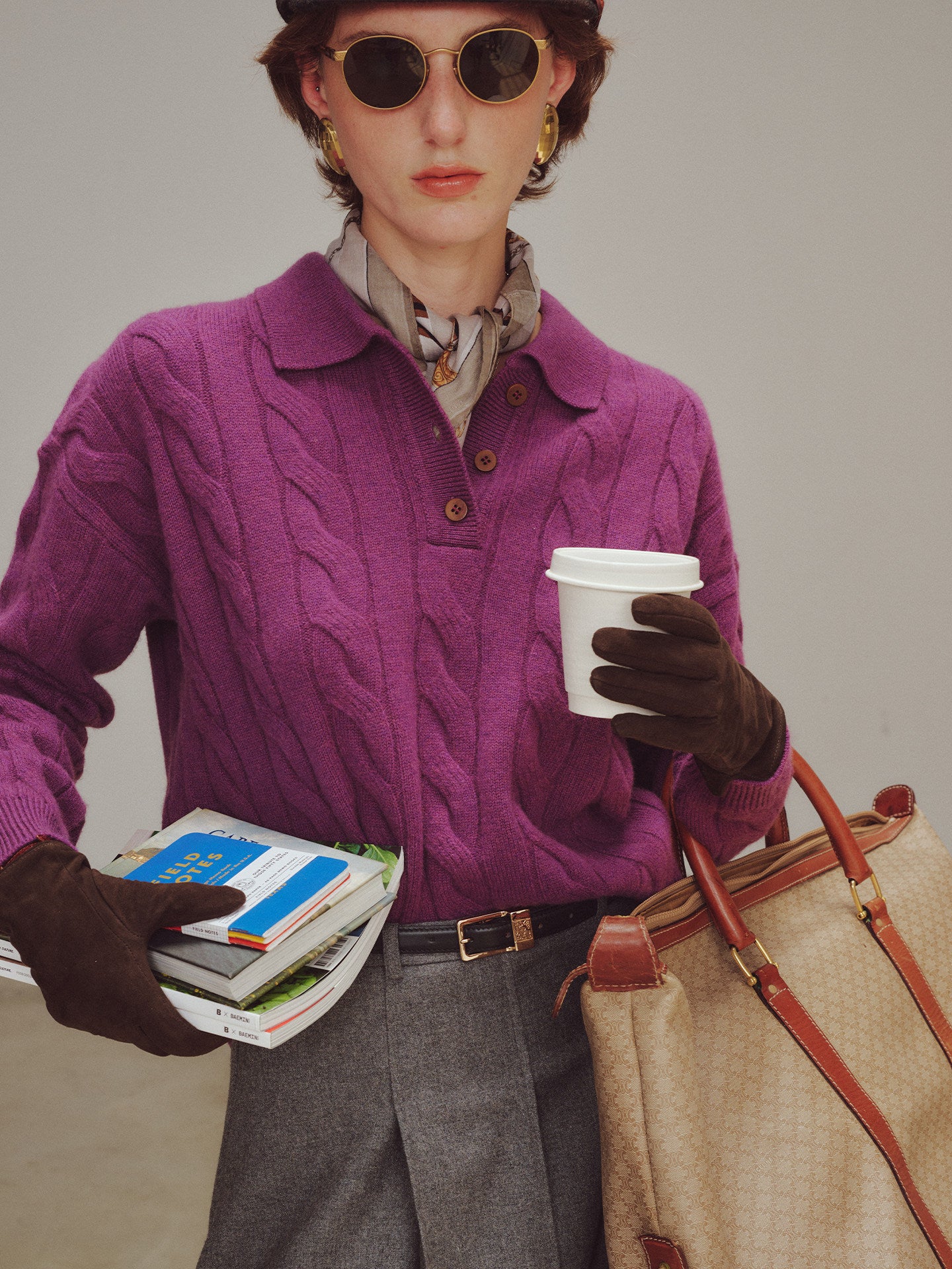Person wearing a purple sweater holding a coffee cup and books, with a beige handbag.