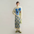 Woman wearing a floral sweater and patterned skirt against a plain background