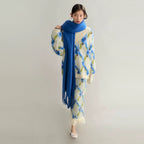 Person wearing a patterned outfit with a long blue scarf against a plain background