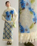 Woman wearing a floral-patterned sweater and skirt with a matching blanket.