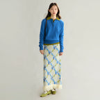 Woman wearing a blue sweater and patterned skirt on a plain background