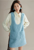 Woman wearing a light blue knitted dress over a white shirt against a neutral background