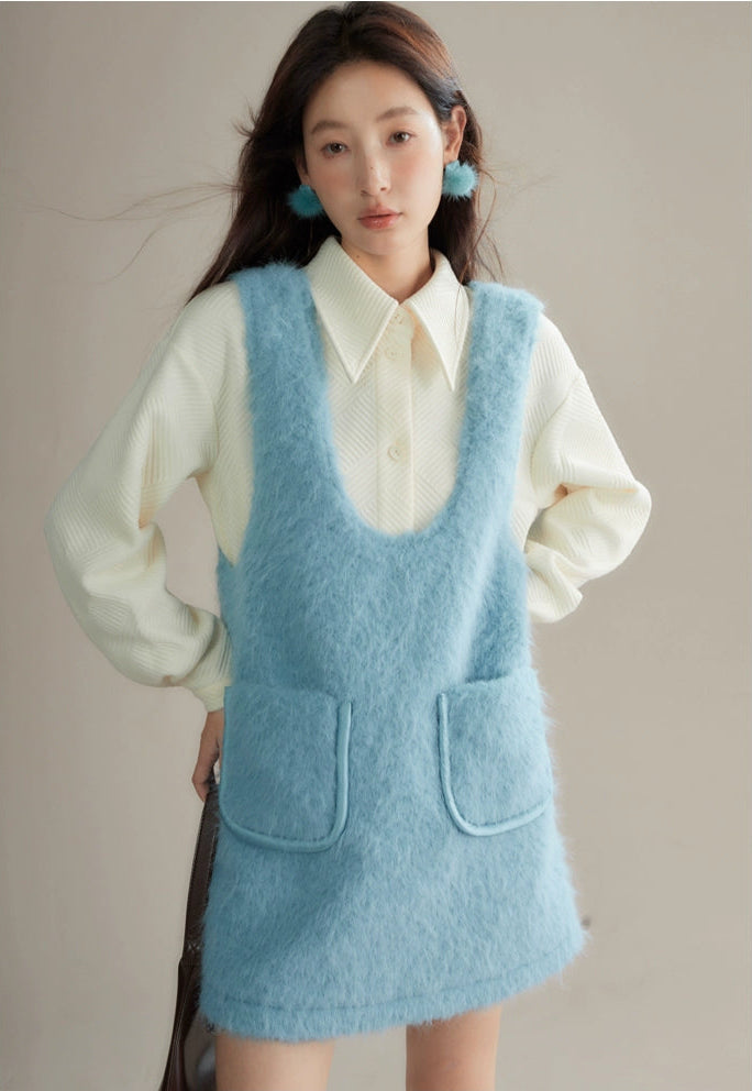 Woman wearing a light blue knitted dress over a white shirt against a neutral background