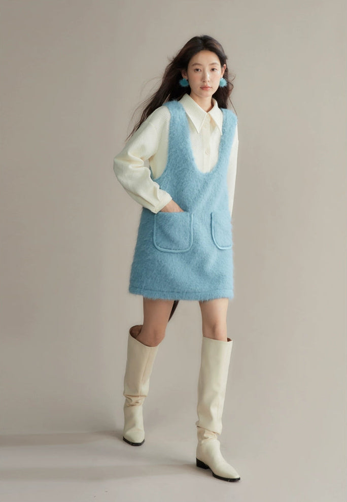 Woman wearing a light blue dress over a white shirt with cream knee-high boots against a plain background