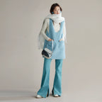 Person wearing a light blue sleeveless top and pants with a white scarf and black handbag on a plain background