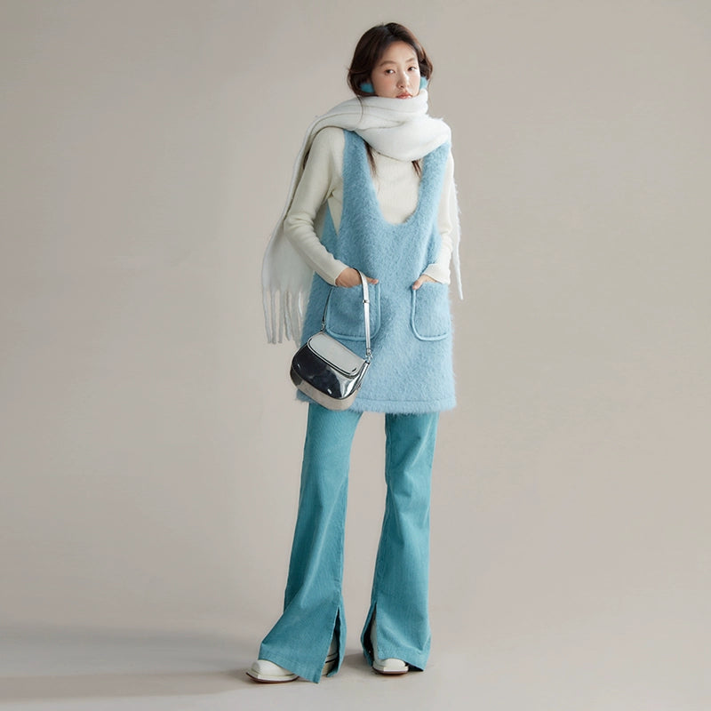 Person wearing a light blue sleeveless top and pants with a white scarf and black handbag on a plain background