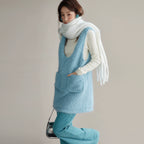 Person wearing a light blue sleeveless vest over a white shirt with a scarf, standing against a plain background.