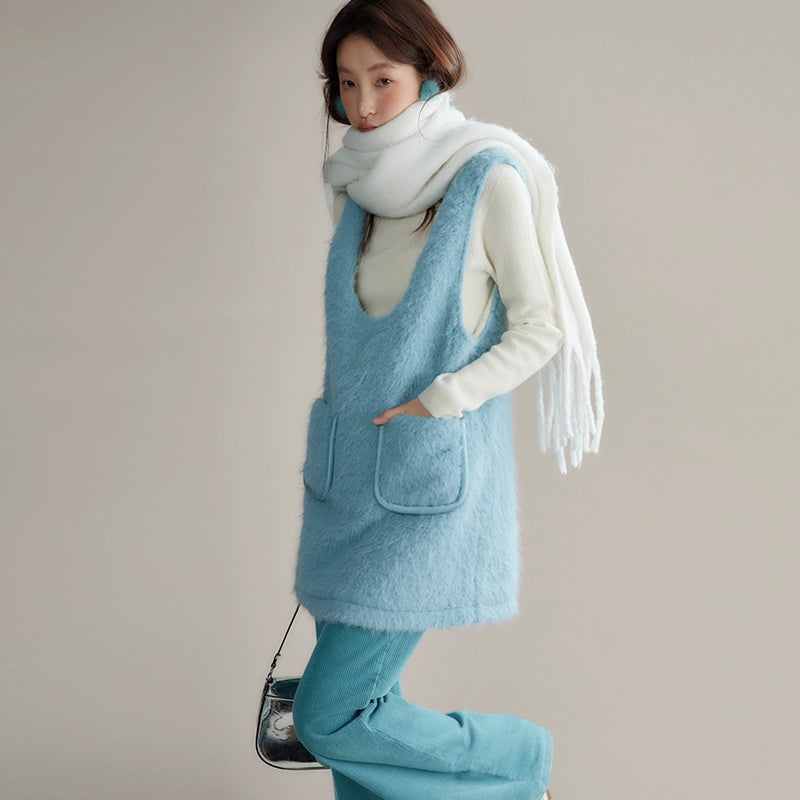 Person wearing a light blue sleeveless vest over a white shirt with a scarf, standing against a plain background.