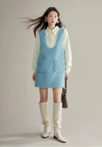 Woman wearing a light blue dress over a white shirt with cream knee-high boots, holding a brown bag.