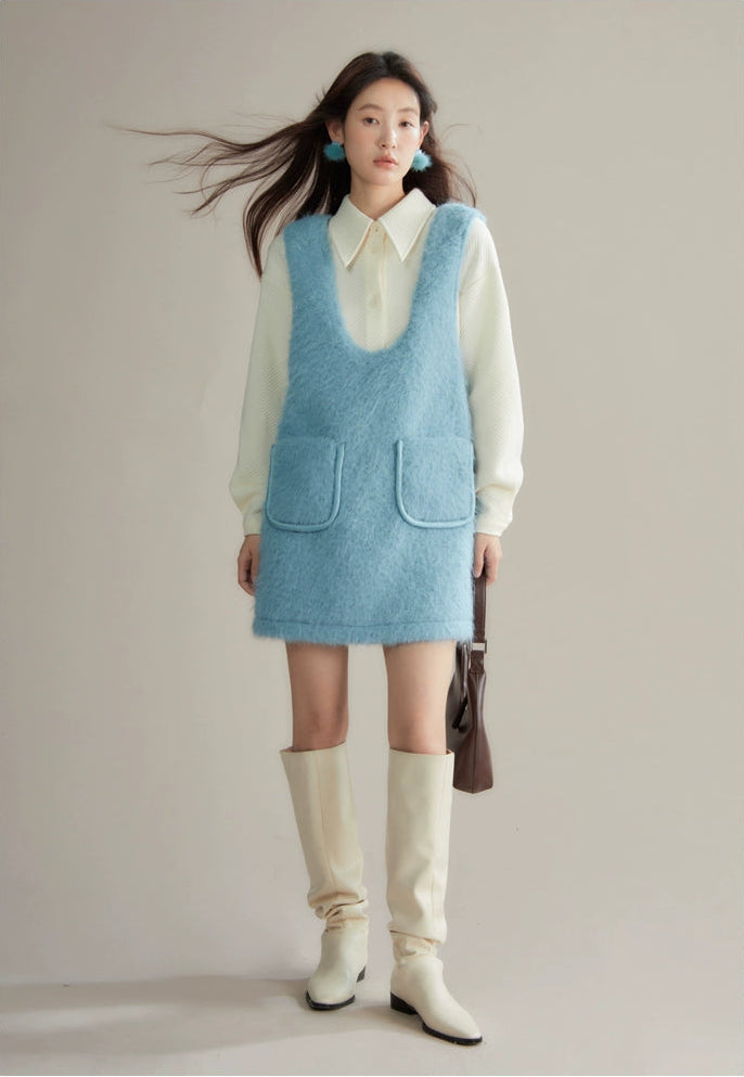 Woman wearing a light blue dress over a white shirt with cream knee-high boots, holding a brown bag.