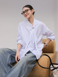 Woman wearing a white blouse and jeans sitting on a brown chair against a gray background
