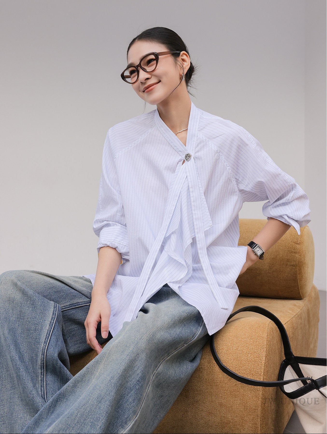 Woman wearing a white blouse and jeans sitting on a brown chair against a gray background