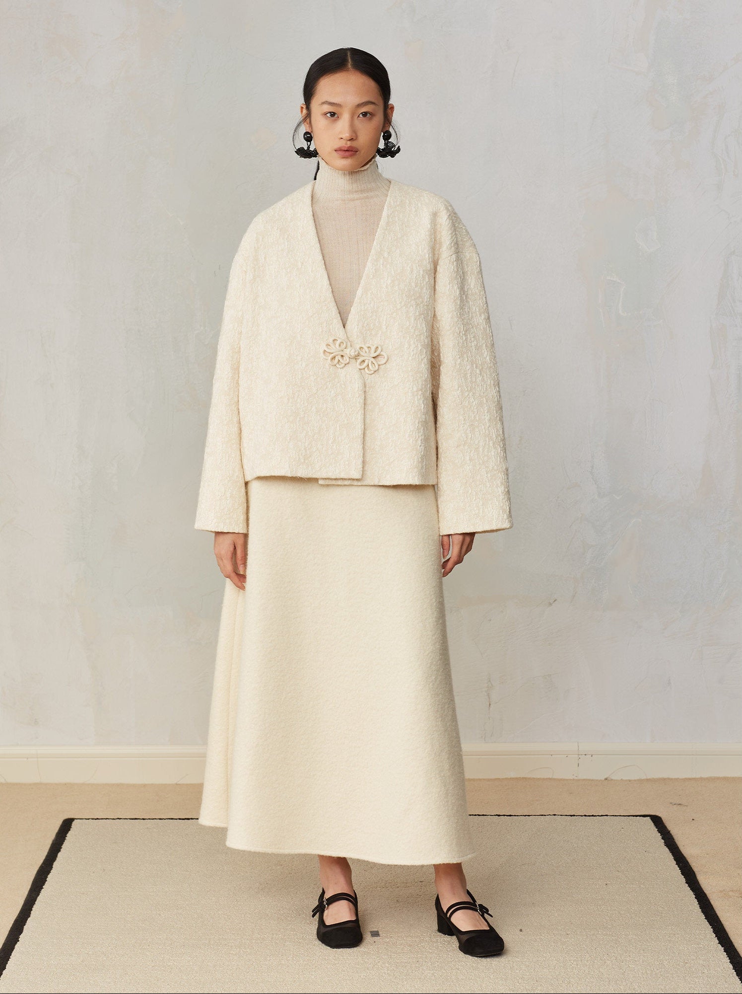 Woman wearing a cream-colored outfit with a textured jacket and skirt against a plain background