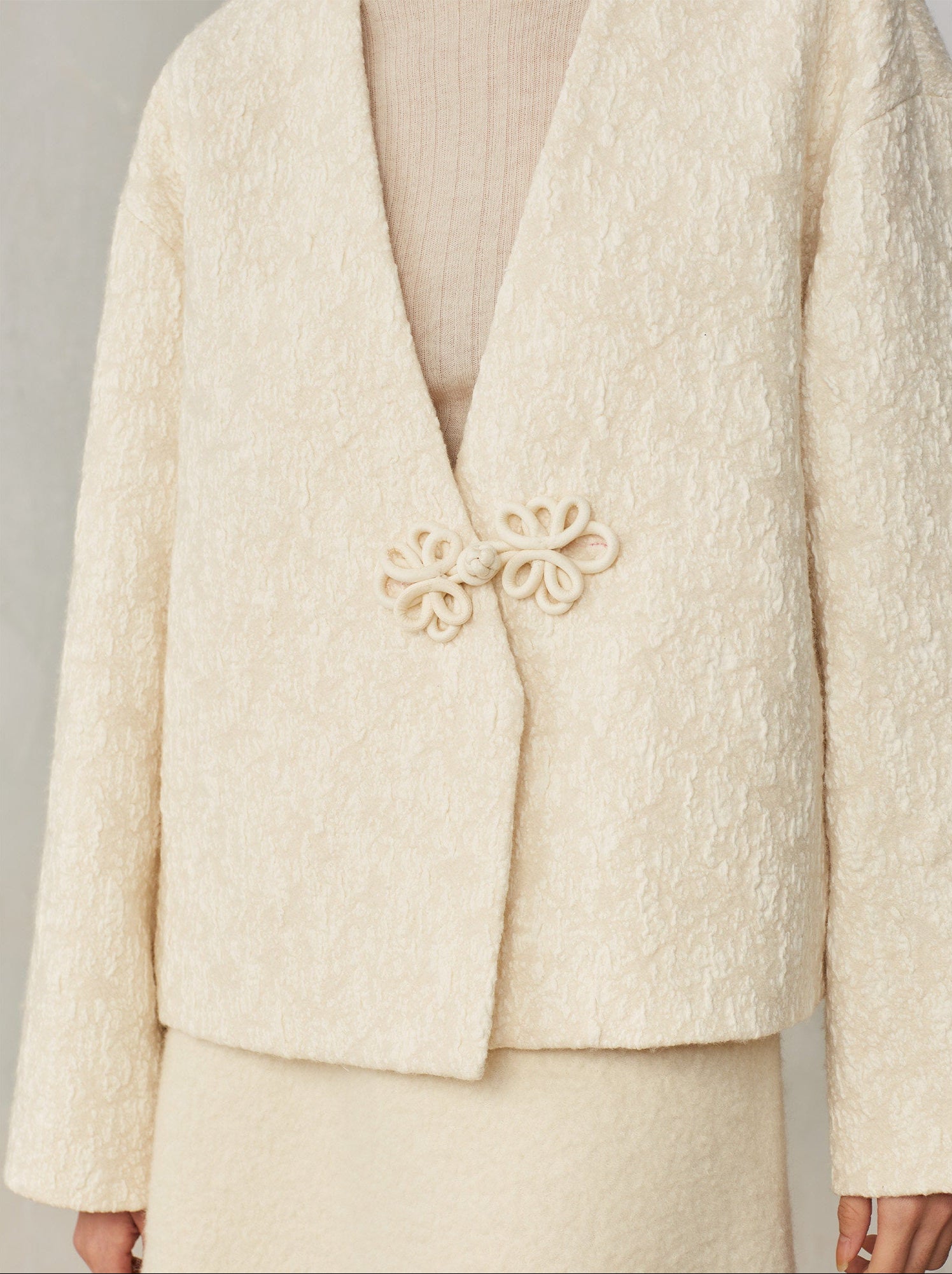 Cream-colored textured blazer with decorative brooch on a neutral background