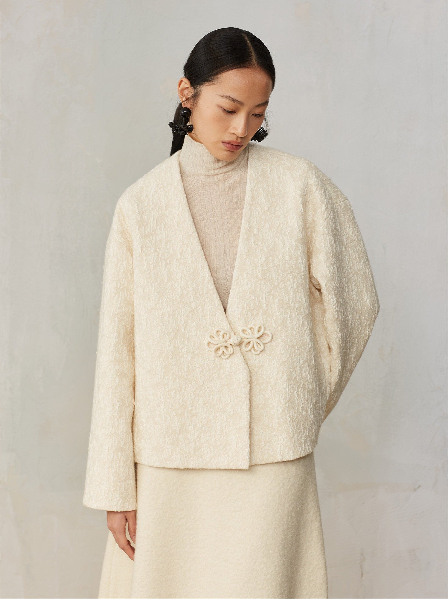 Woman wearing a cream-colored outfit with a textured jacket against a plain background