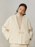 Woman wearing a beige textured jacket with a floral brooch on a plain background