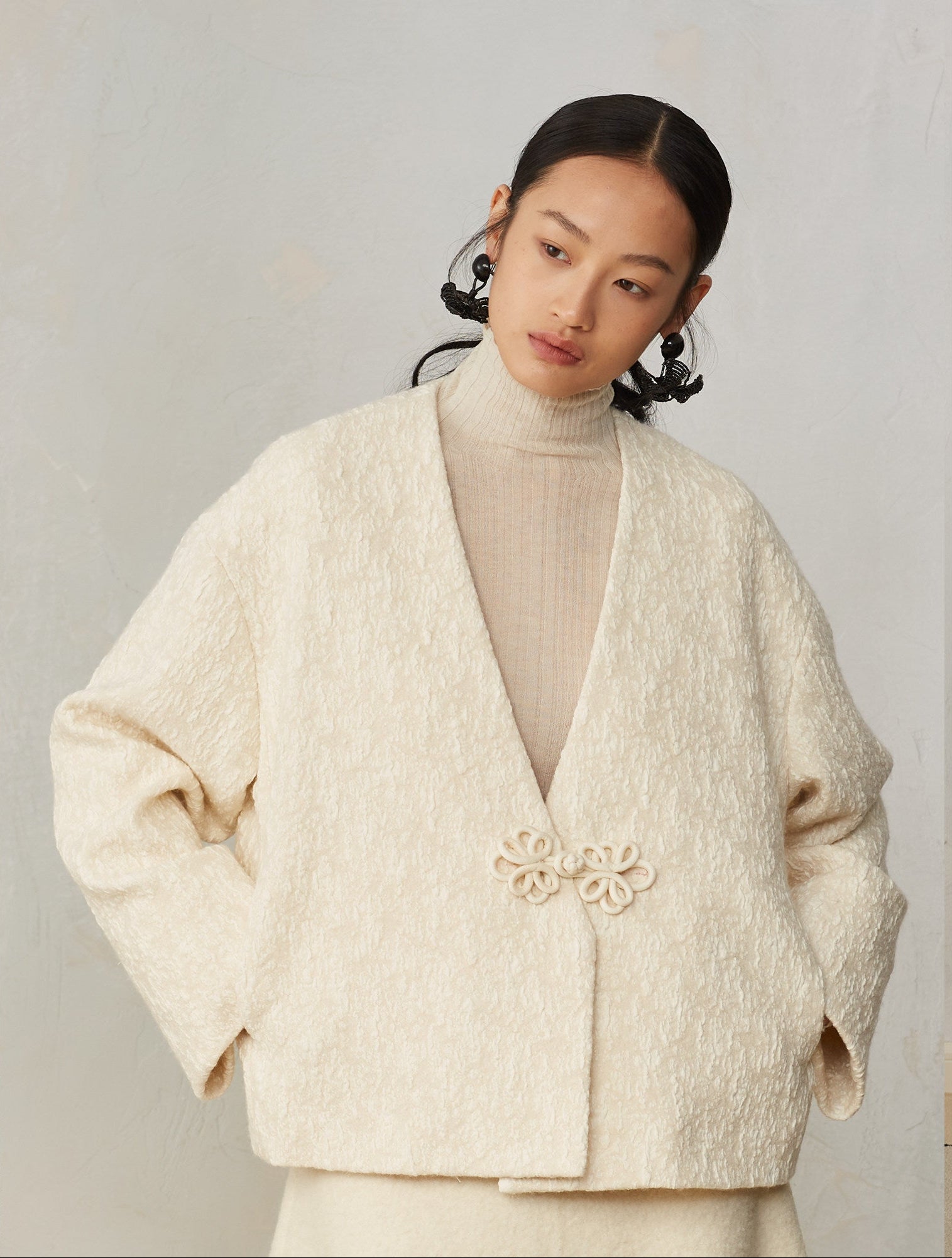 Woman wearing a beige textured jacket with a floral brooch on a plain background