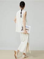 Woman in a white sleeveless top and pants holding a magazine against a plain background