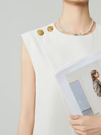 Person wearing a white sleeveless top with gold buttons, holding a photo of a woman.