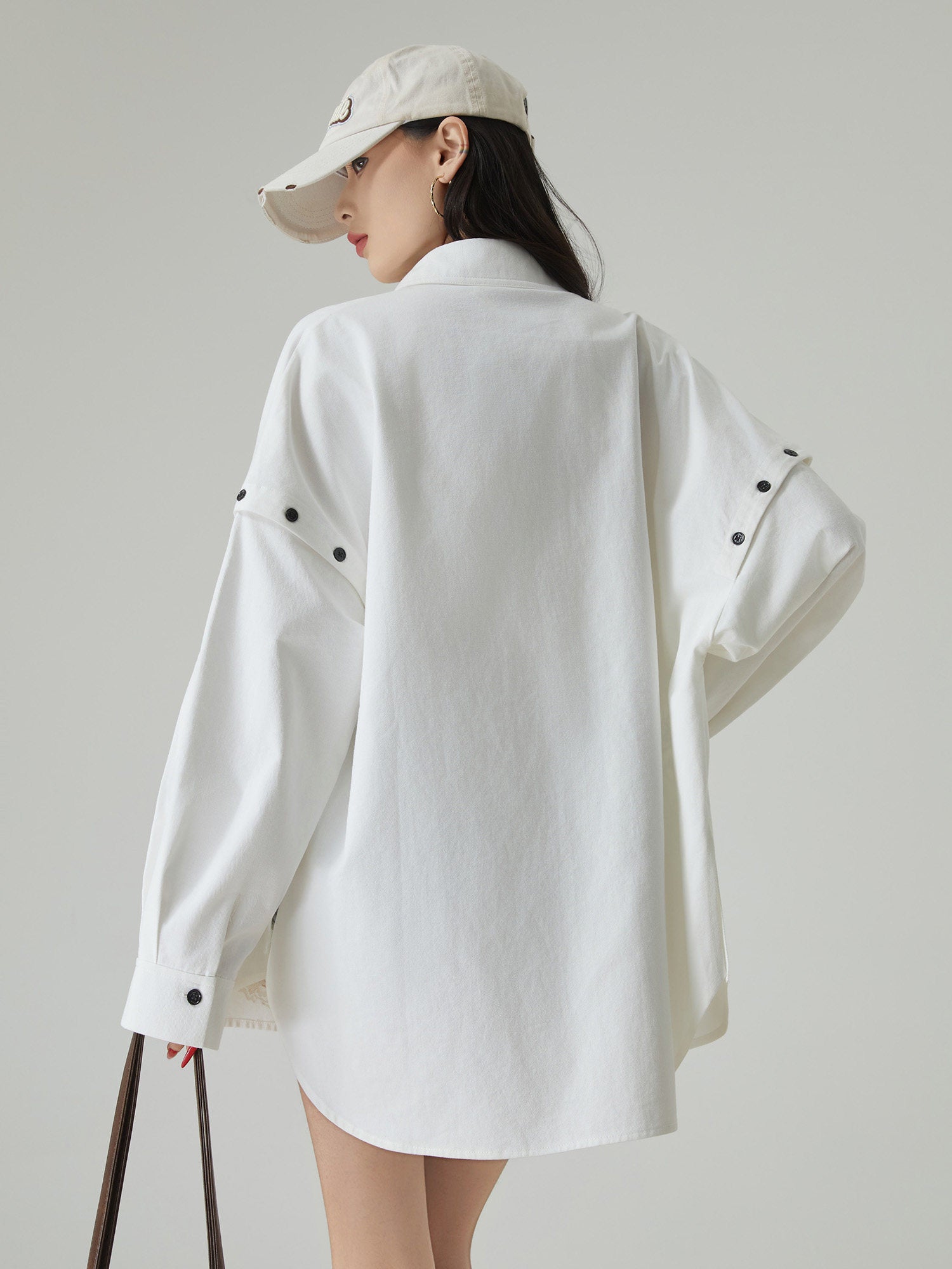 Person wearing a white oversized shirt and beige cap on a plain background