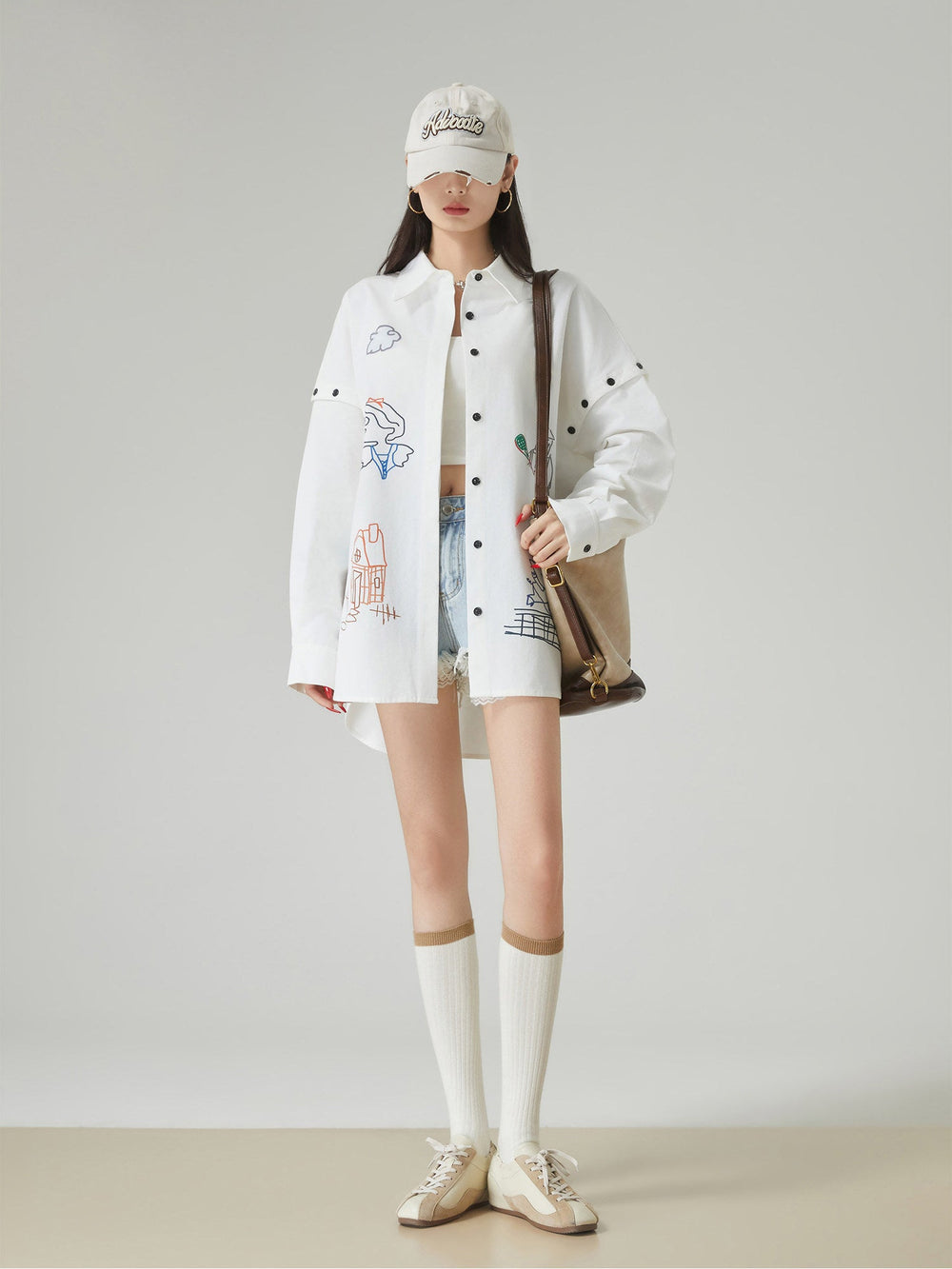 Person wearing a white jacket with colorful designs, shorts, and knee-high socks on a plain background