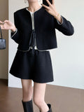A person wearing a black textured tweed short jacket and matching shorts set with white piping trim, paired with a white top and black knee-high boots, shown in a mirror selfie.