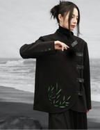 Person wearing a black coat with green leaf design against a gray background