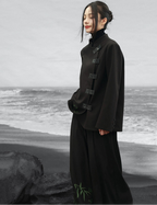 Person wearing a black coat standing on a beach with ocean waves in the background