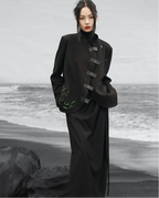 Person wearing a black coat on a beach with gray water and rocks.