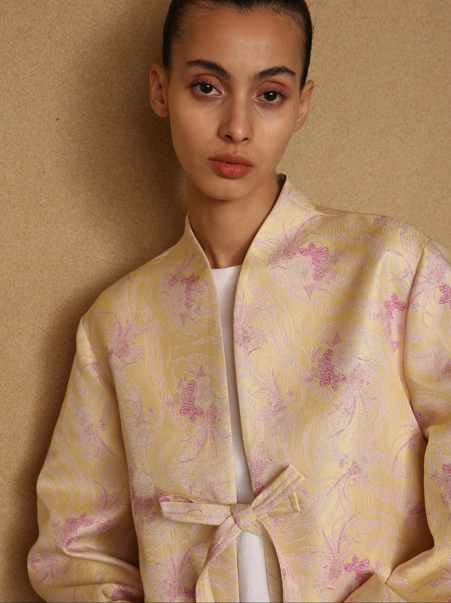 Woman wearing a light yellow floral patterned outfit against a beige background