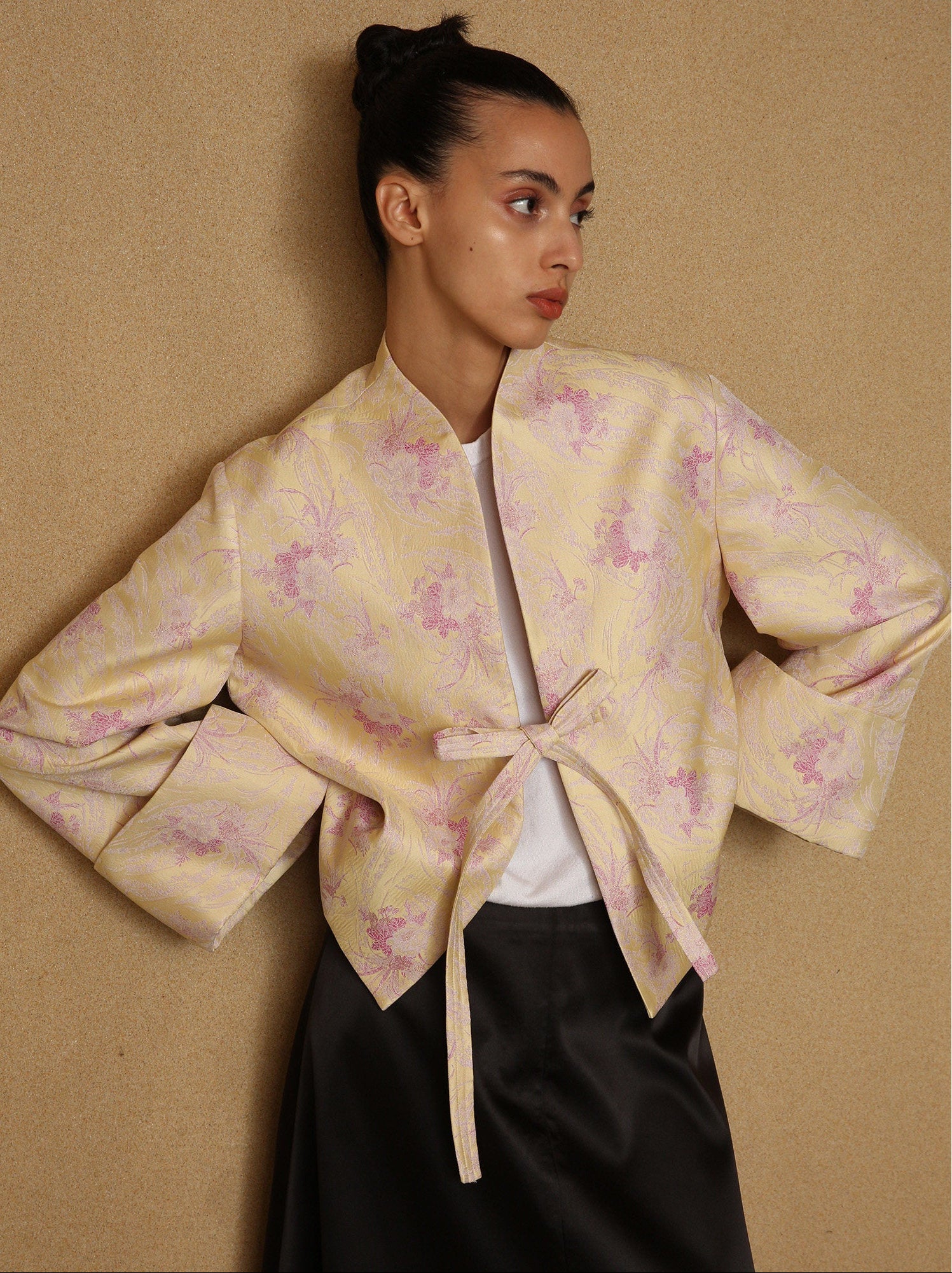 Woman wearing a light-colored floral blouse with a tie detail against a beige background