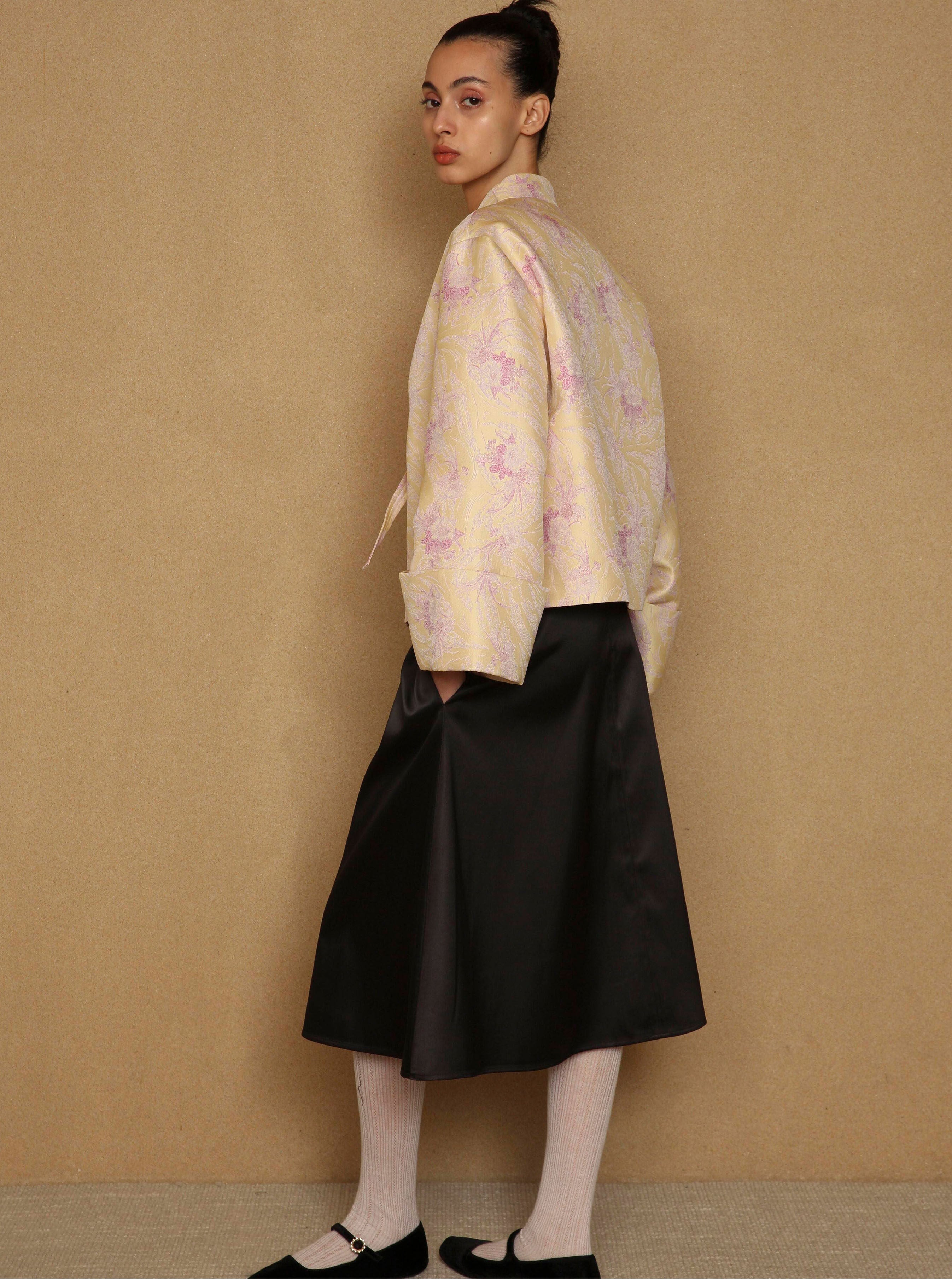Woman wearing a light-colored floral blouse and black skirt against a beige background