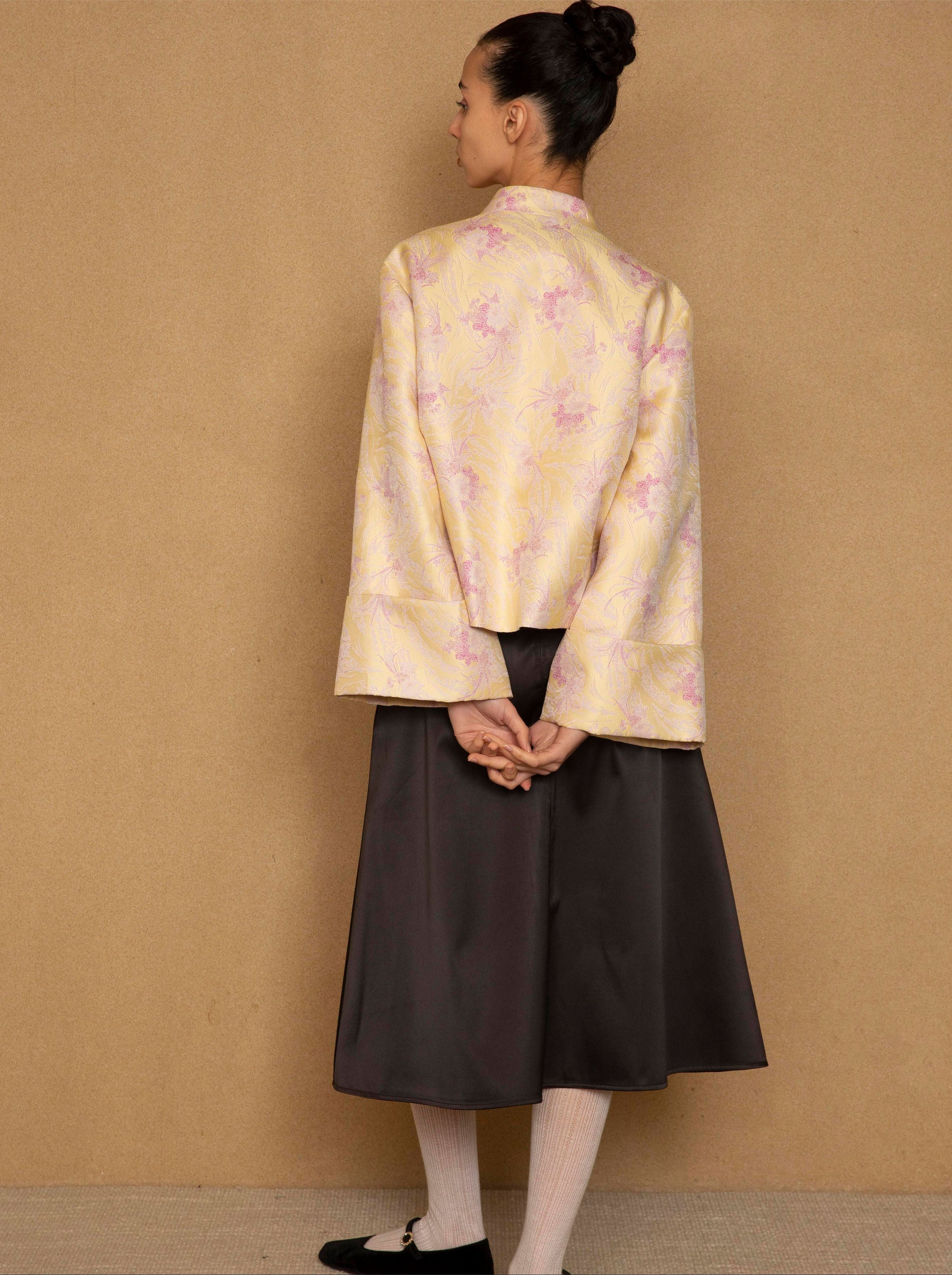 Woman wearing a light-colored floral jacket and dark skirt against a beige background