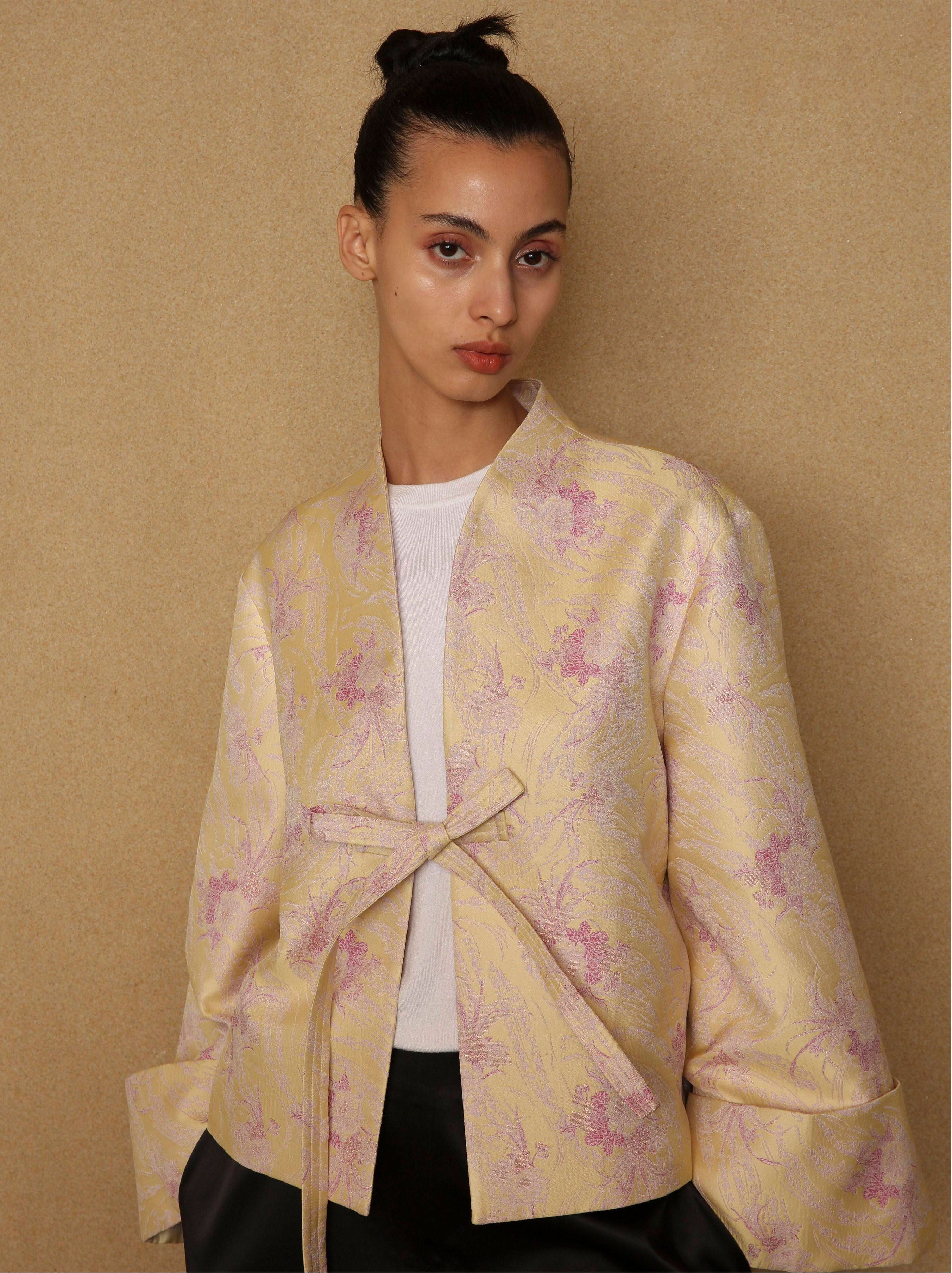 Woman wearing a yellow floral jacket against a beige background