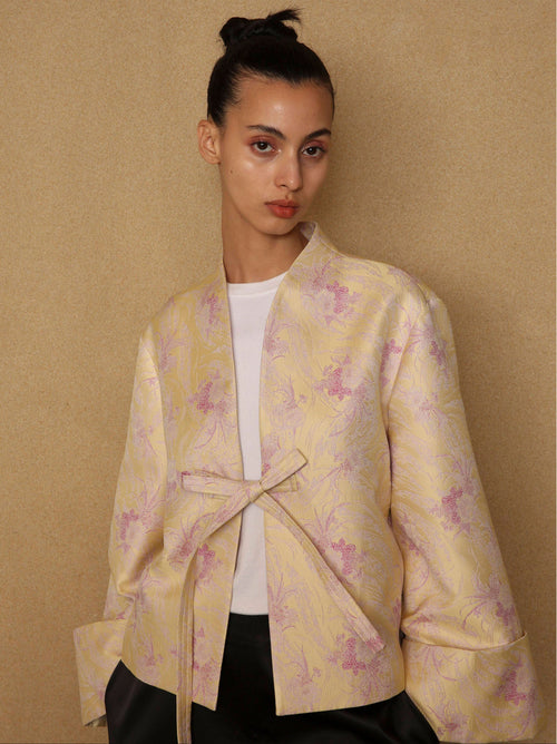 Woman wearing a yellow floral jacket against a beige background